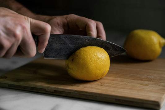 A chef uses the pinch grip technique to slice a fresh lemon on a wooden cutting board.