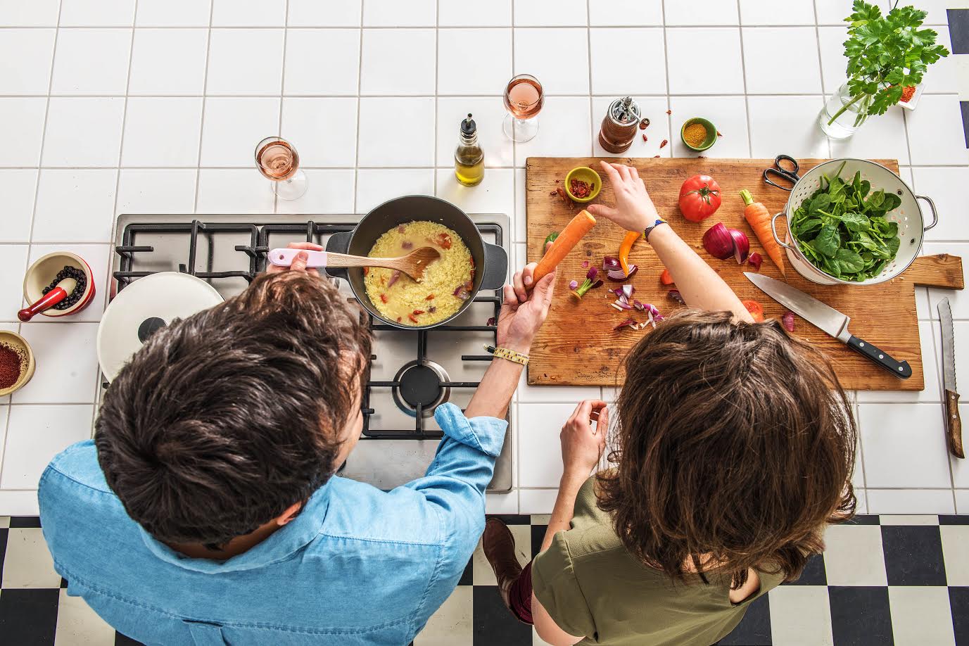 Two people cooking together in a kitchen with ingredients and utensils on the counter.