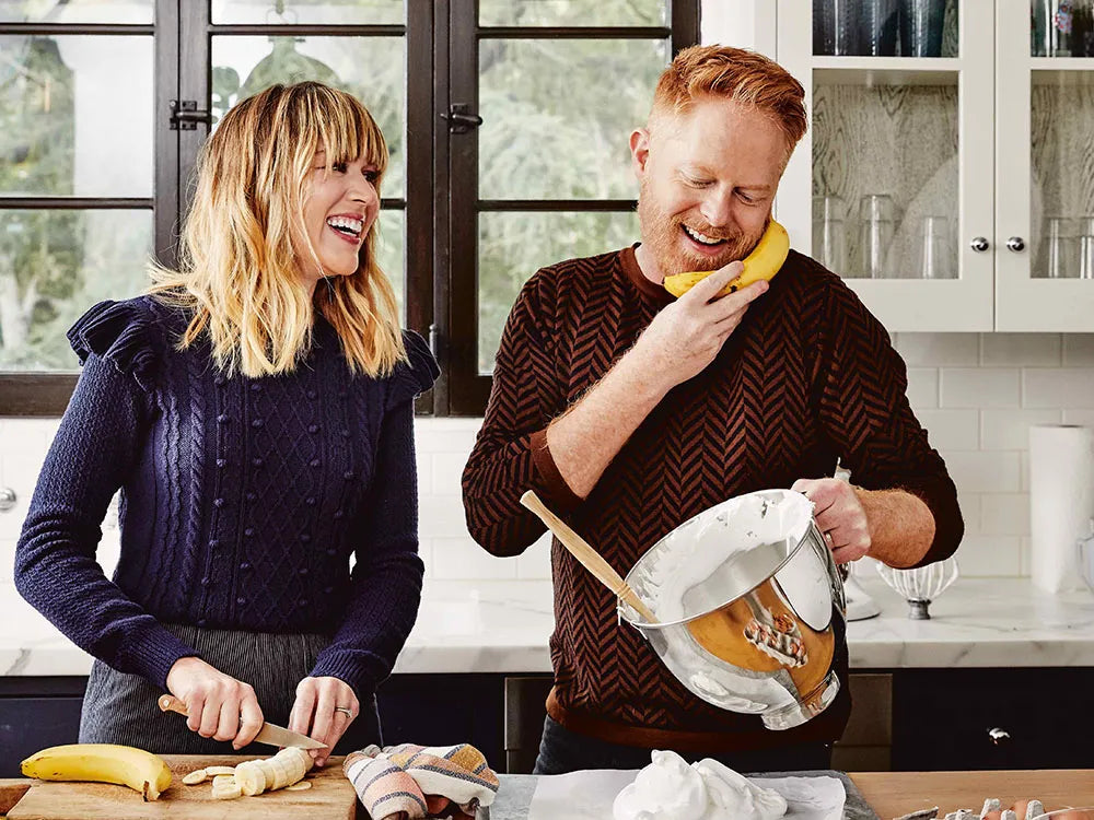 Two friends cooking together in a bright kitchen, smiling as they prepare food, with sharpened knives from Sharpen Up 365 on the counter.