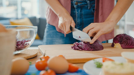 Hand of young woman holding knife cutting red cabbage on wooden board on kitchen table 