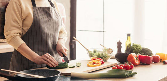 Woman cooking at kitchen, panorama view. Slicing cucumber with sharp knife.