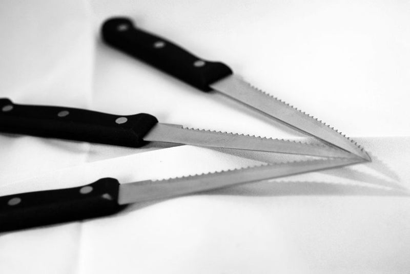A black and white photograph of three serrated knives arranged together