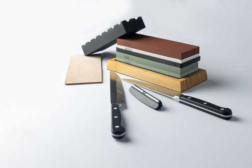 white background on stand lies all the equipment a set for sharpening and polishing kitchen knives and various blades different abrasiveness of stones retainer for knives sheet tanned leather knives
