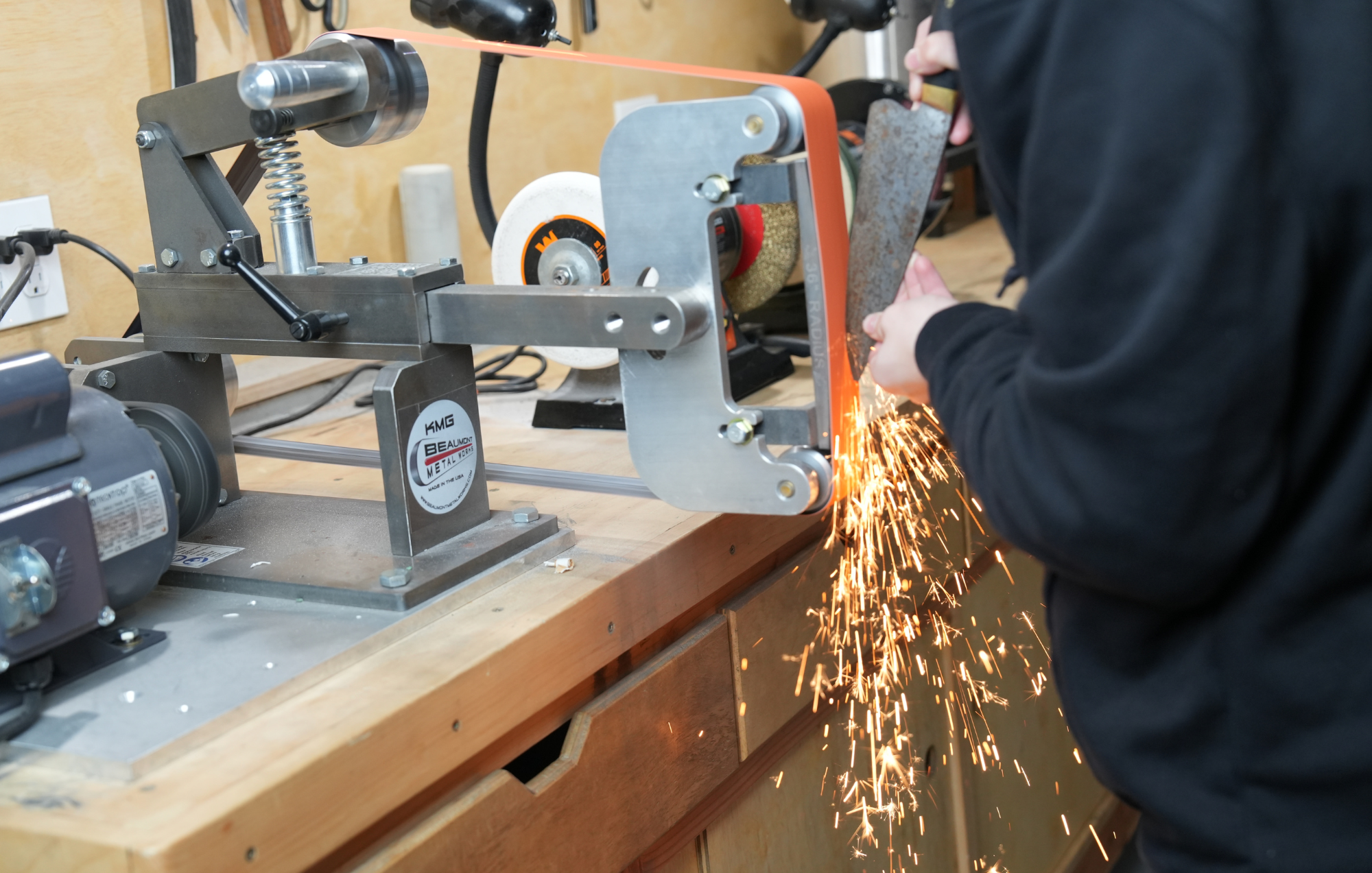 Person using a belt sander with sparks flying in a workshop setting