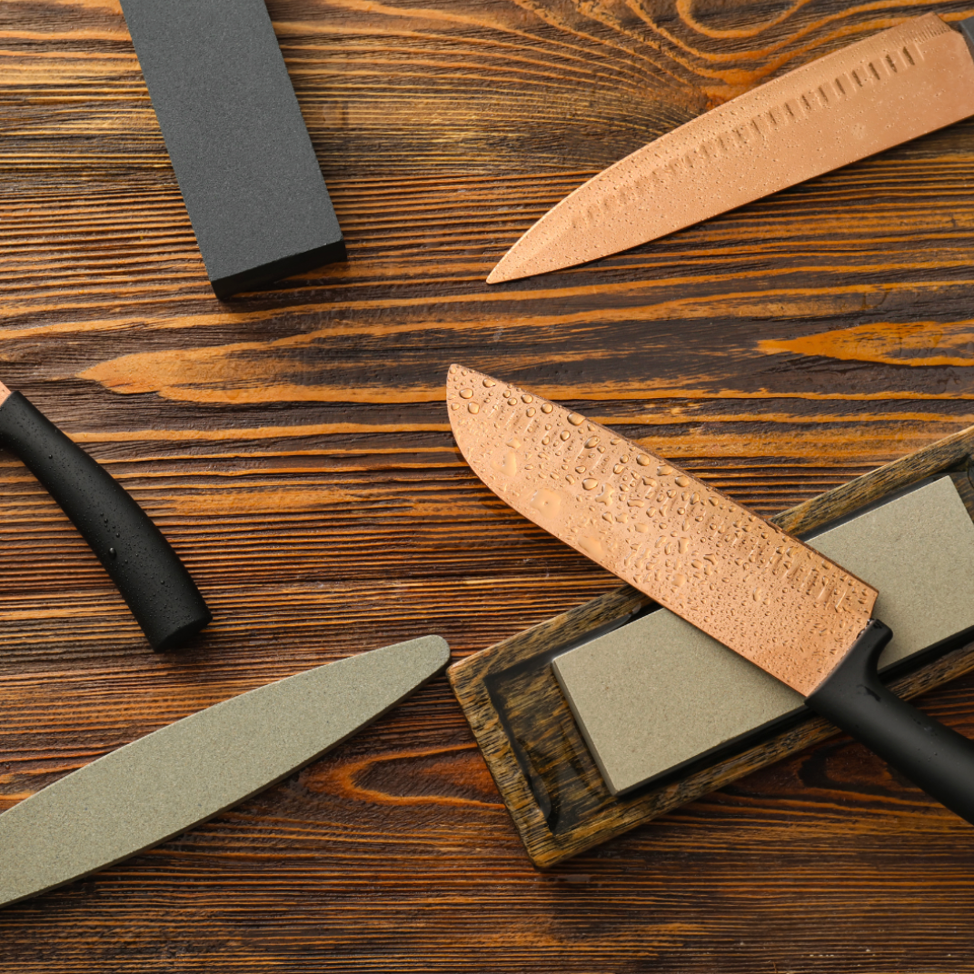 Several kitchen knives arranged beside a whetstone on a clean white surface, ready for sharpening.